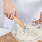 Hands using an oak-handled coil whisk to mix batter in a bowl