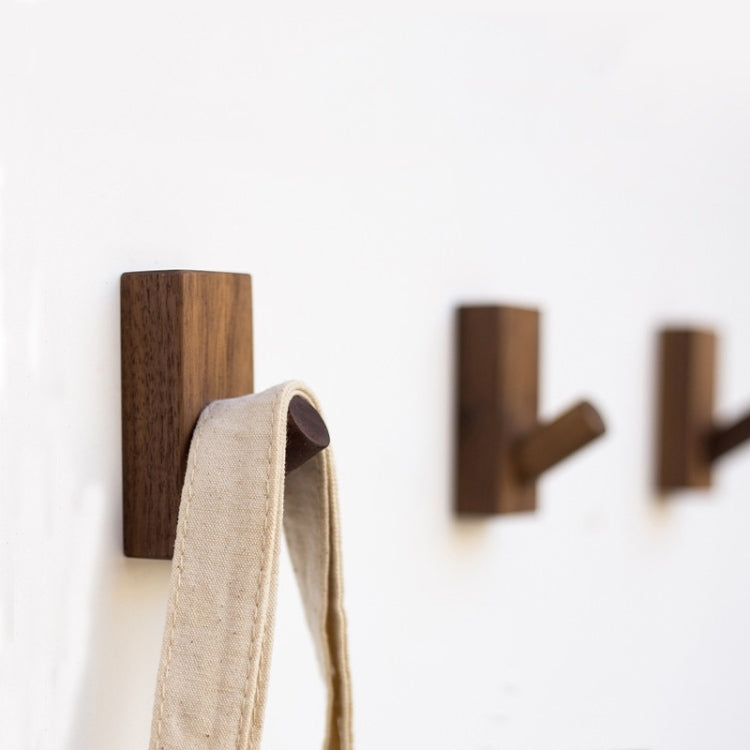 Dark wood wall hook with rounded peg holding a beige strap