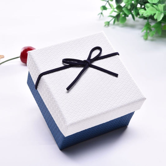 Small jewelry gift box with white lid, blue sides, tied with dark navy ribbon bow.