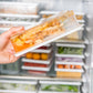 Hand holding a rectangular refrigerator storage container with lid inside an open freezer