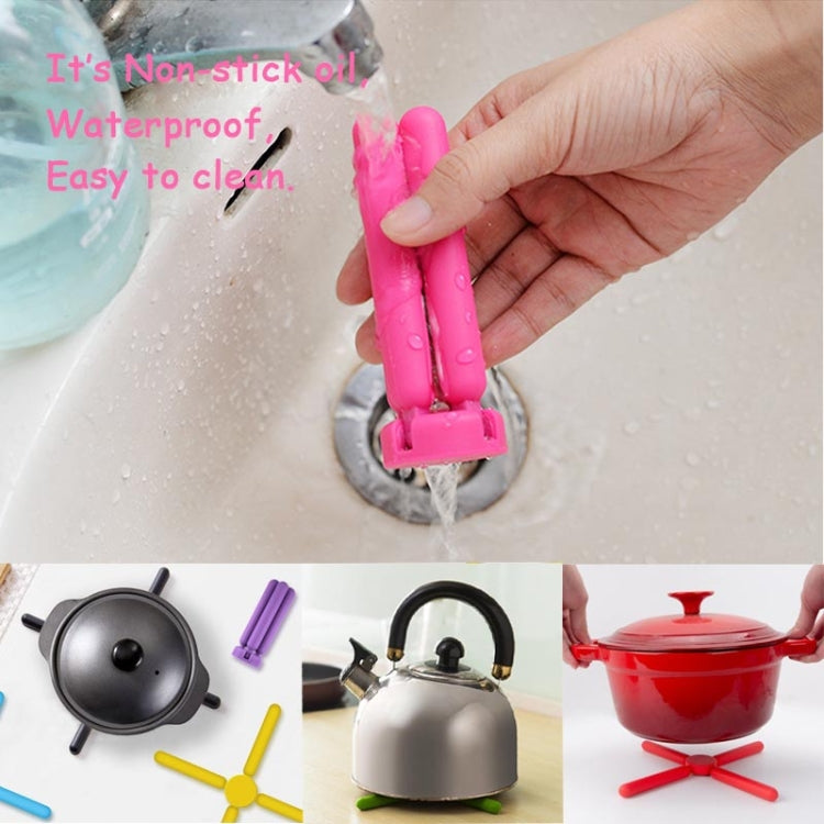 Pink cross-shaped folding silicone pot mat being rinsed under water for easy cleaning.