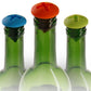 Three screw-style silicone bottle stoppers on glass bottles: blue, orange, green