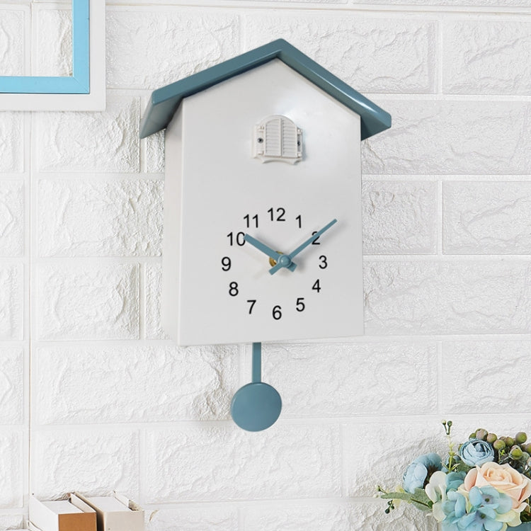 White cuckoo wall clock with blue hands, gray top, pendulum weight, and bird compartment