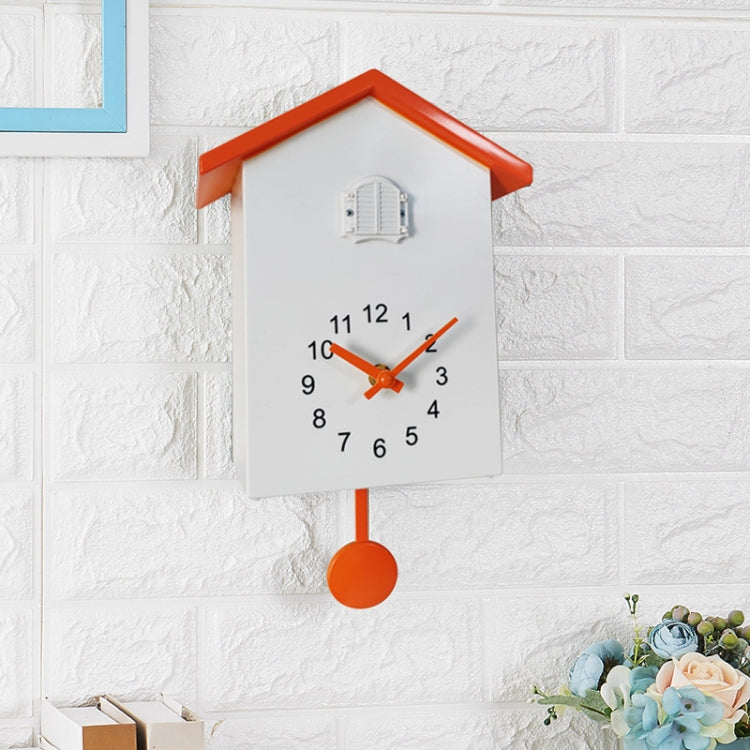 White cuckoo wall clock with orange hands, orange top, pendulum weight, and bird compartment