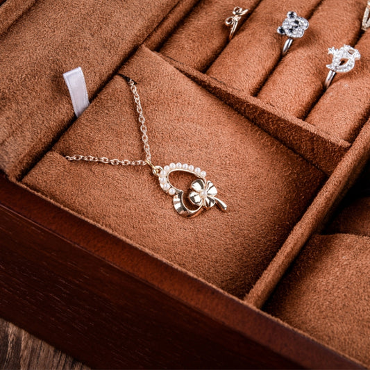 Close-up of jewelry in a brown wooden watch box with tan padded inserts