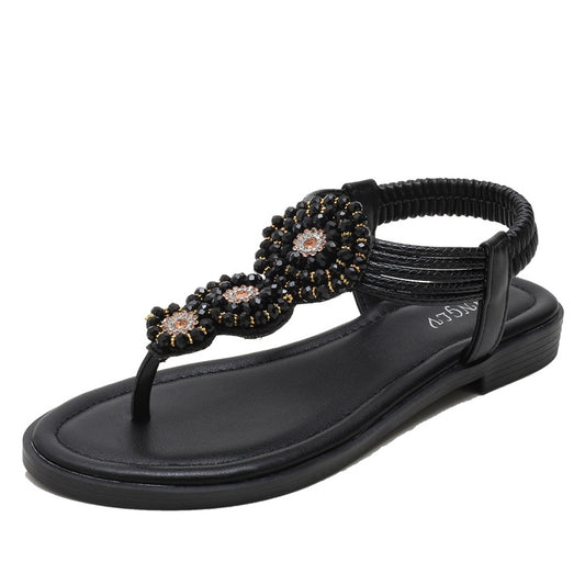Black flat thong sandals with ornate beaded floral decoration across the straps