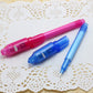Set of UV invisible ink pens: pink, blue, and light blue with translucent caps.