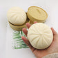 Squishy cream bun in hand; tan bun toy pieces in round storage tins