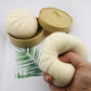 Hand squeezing cream squishy bun toy; tan bun pieces in open round tins