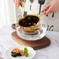 Gold stainless steel melting bowl on a glass base, with long handle and side loop grips