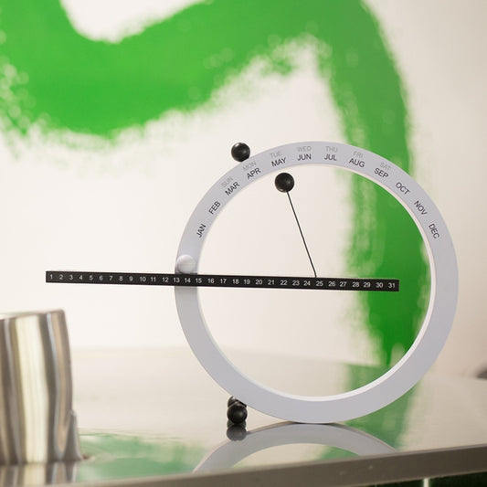 White circular calendar ornament with month markers, black pointer arm and pegs.