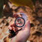 2-in-1 outdoor compass held in hand; clear body with black braided lanyard