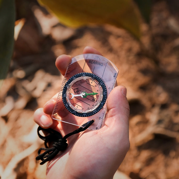 2-in-1 outdoor compass held in hand; clear body with black braided lanyard