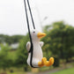 Duck car pendant hanging from black cords; white body with yellow beak and feet
