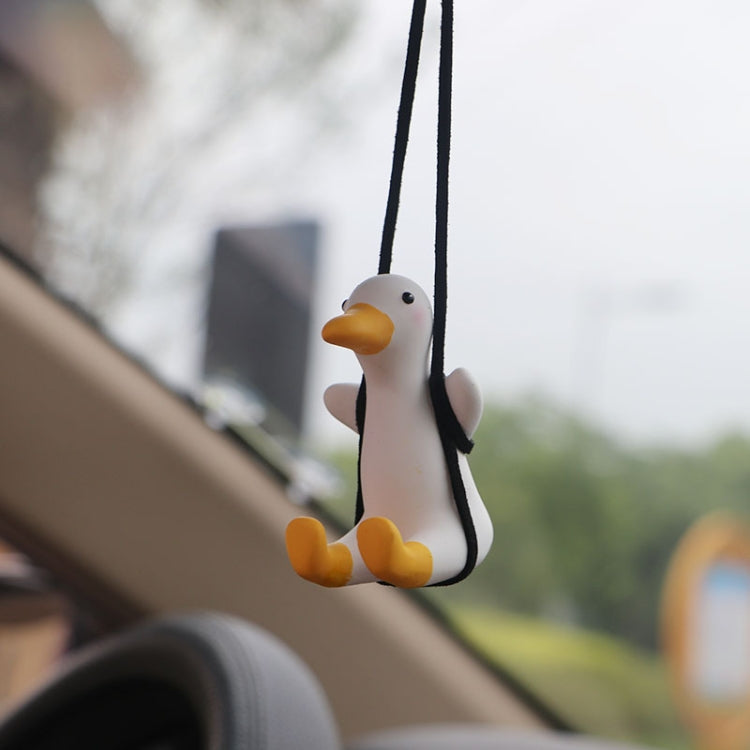 Small white duck car pendant hanging from two black cords, yellow beak and feet