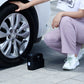 Portable black electric car air pump on pavement beside car wheel and charging cable