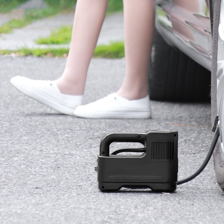Portable black car inflatable air pump with hose on driveway near car wheel