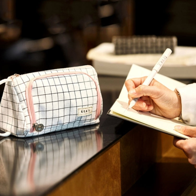 Canvas pencil case on desk with hand holding a pen; white grid pattern with pink zipper trim