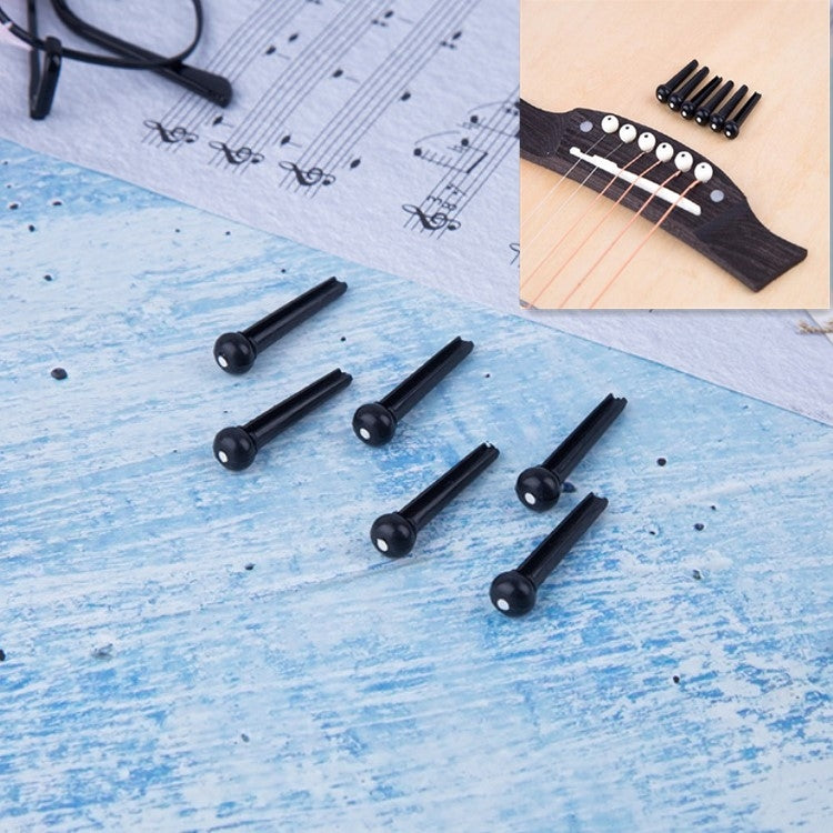 Black guitar string nails with plastic conical heads, shown as a set on blue paper