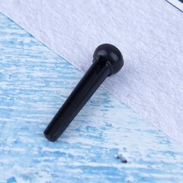Black plastic guitar string nail with conical head, angled view on blue paper