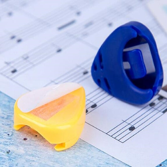 Yellow guitar pick storage box with open slot, sitting on sheet music and blue pick container.