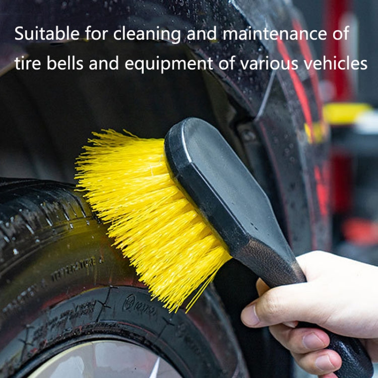 Tire cleaning brush with yellow bristles scrubbing a rubber tire surface