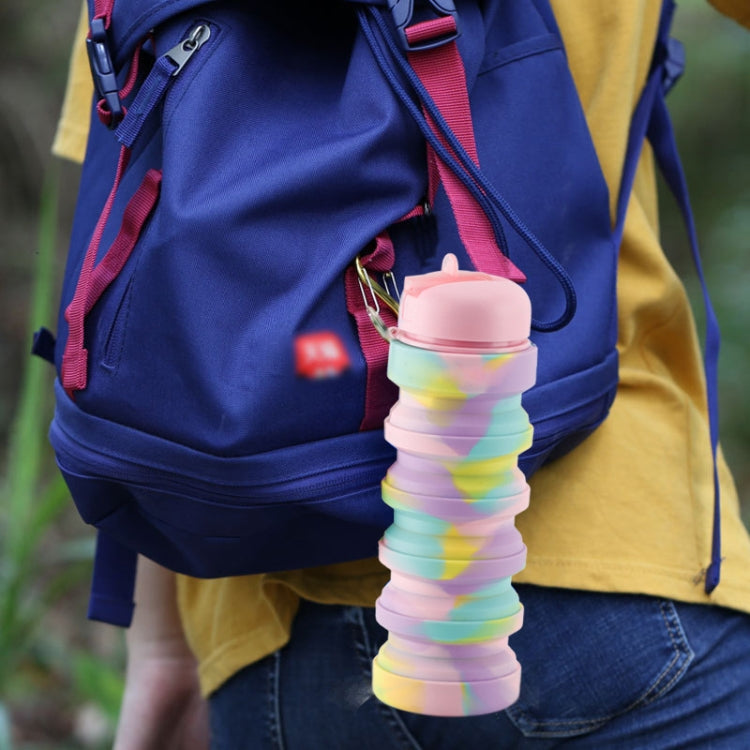 Collapsible rainbow silicone water cup clipped to a backpack with pink top