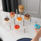 3-tier clear acrylic cake display stand with silver posts holding assorted mini cakes