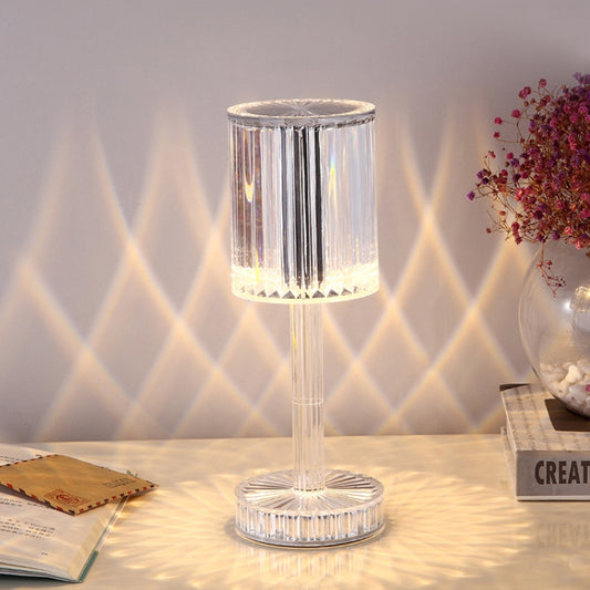 Clear cylindrical crystal table lamp with faceted acrylic shade, glowing warm white