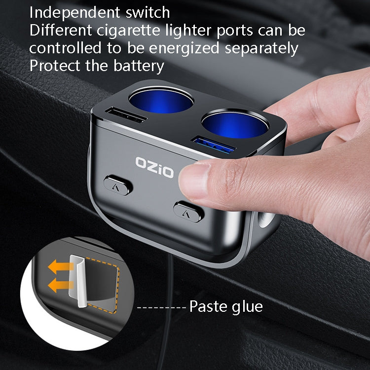 Ozio dual-USB car charger inserted in socket with hand, switches, and two blue ports