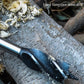 Punch drill bit tool drilling into a log, with brown leather case