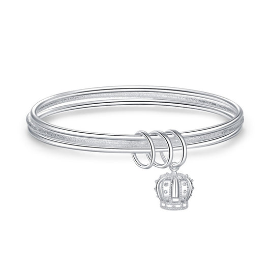 Silver three-ring bracelet with crown charm detail and triple loop clasp, angled view.