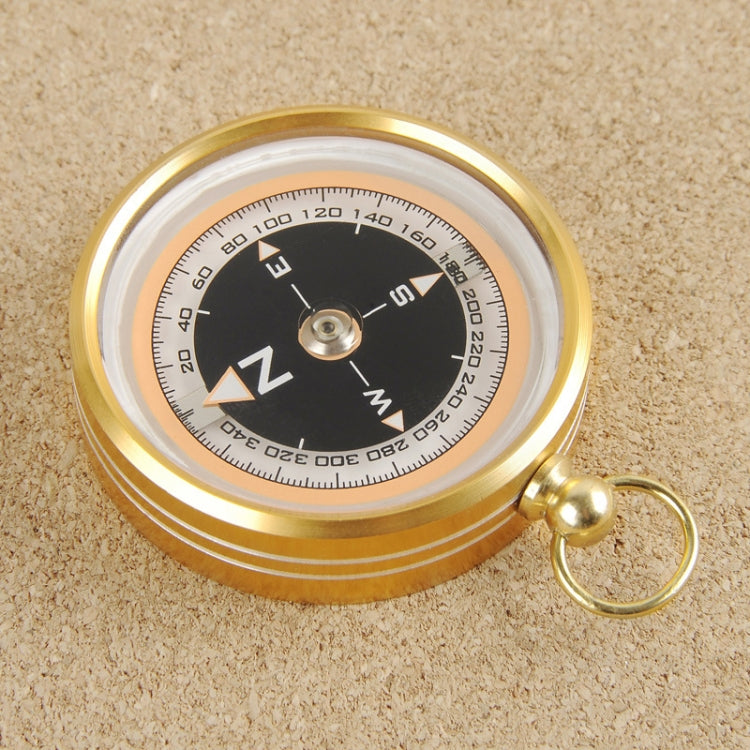 Gold portable compass on textured surface, black dial and keyring loop visible.