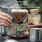 Stainless steel folding coffee filter funnel set on glass carafe with paper filter