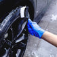 Black bristle cleaning brush scrubbing a tire wheel with a gloved hand