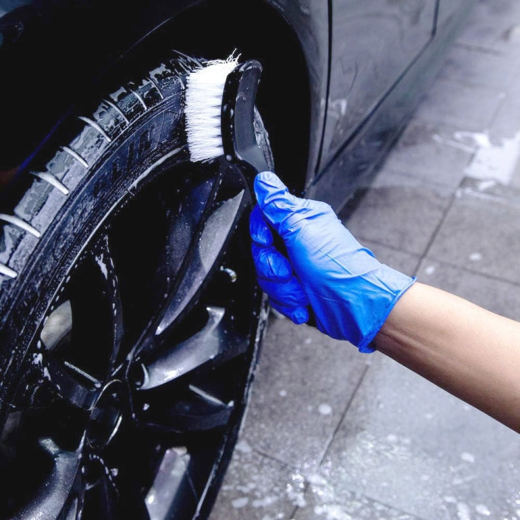 Black bristle cleaning brush scrubbing a tire wheel with a gloved hand