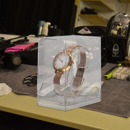 Transparent rectangular watch display box with pull-out holder and wristwatch behind clear lid.