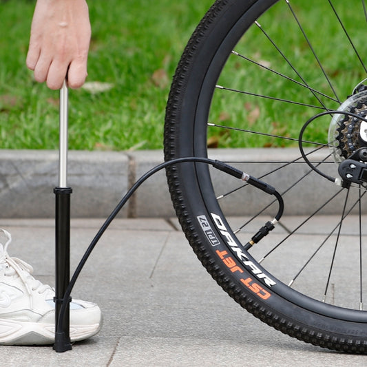 Portable high-pressure bicycle pump standing beside a bike wheel, black body and hose