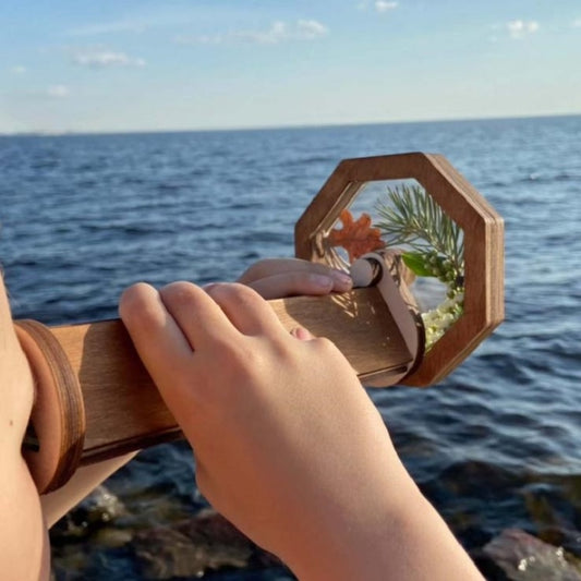 Wooden rotating kaleidoscope toy with octagon window, held in hand outdoors