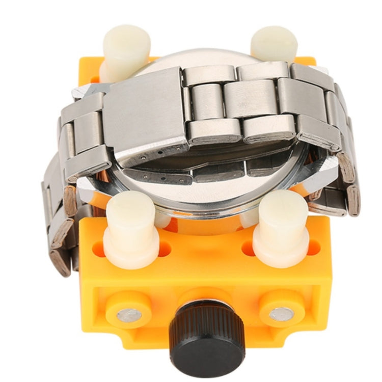 Yellow watch repair tool holding a metal watch case and movement section