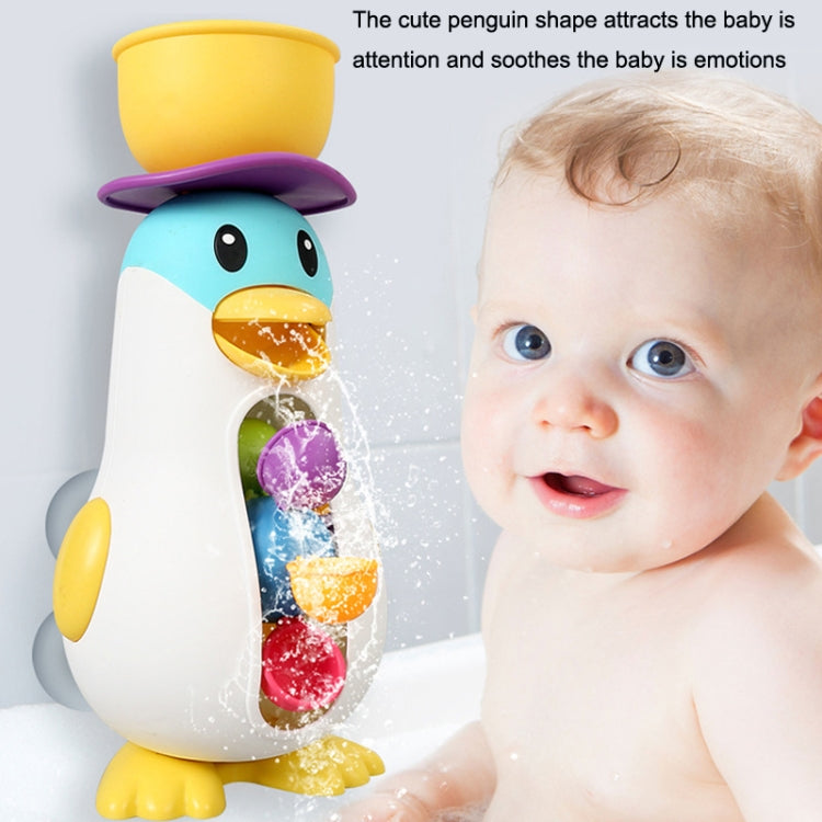 Baby penguin bath water toy with yellow top beside a smiling baby