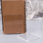 Brown notebook and clear acrylic L-shaped bookend set on bookshelf