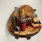 Wall-mounted barrel-style wooden wine rack with black strap holding assorted wine bottles.