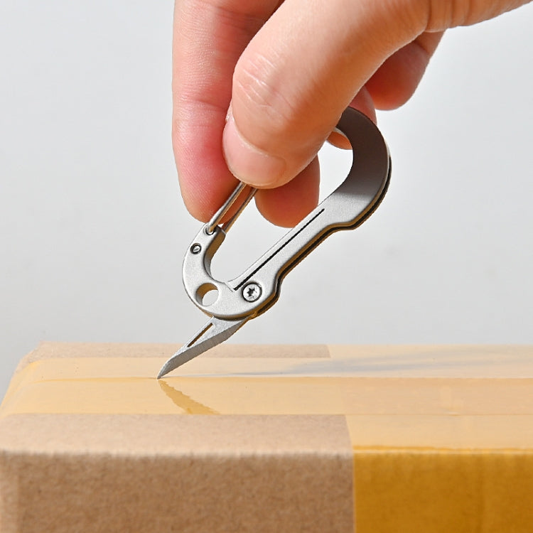 Silver keychain knife cutting cardboard with blade extended