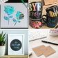 Colorful vinyl cutout designs on paper, plus decor on mugs and framed art