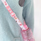 Pink bottle with adjustable shoulder lanyard strap on light blue knit fabric