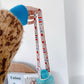 Patterned bottle shoulder strap with turquoise drink bottle on indoor setting