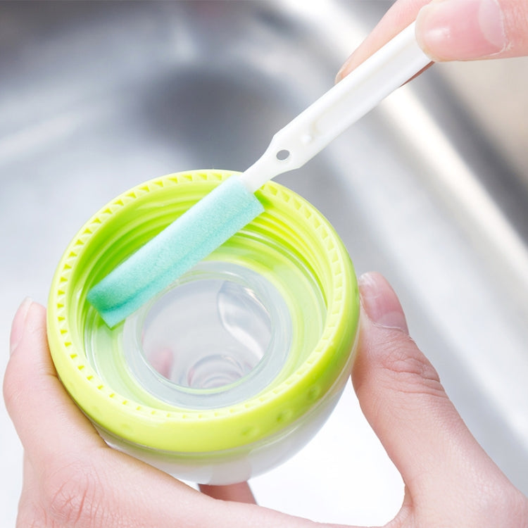 Crevice cleaning brush scrubbing a small cup; light-blue foam pad and green bristles