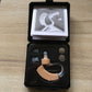 Opened black case with beige hearing aid, ear tips, and round accessory buttons