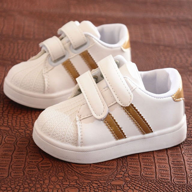 Children's white sneakers with gold side stripes and double hook-and-loop straps, pair